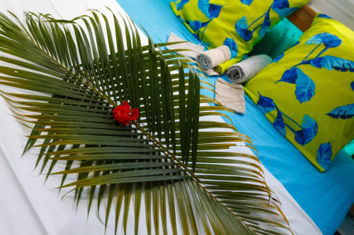 Frondes de palmier et fleur rouge près de coussins à motifs de feuilles jaunes à la piscine de Kaz A Bibi