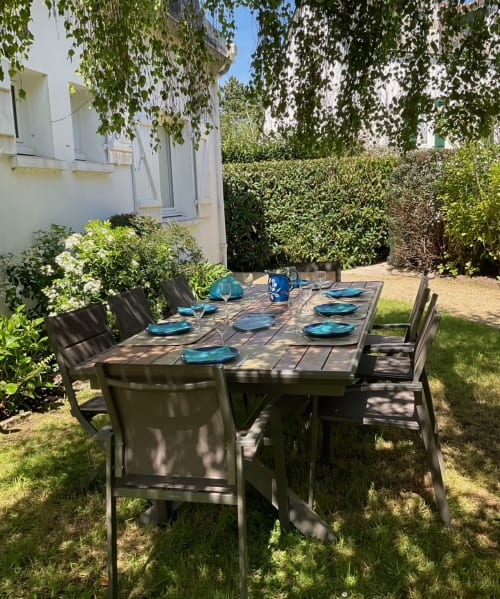 Espace de repas en plein air dans le jardin de la villa Mer et Maisons, La Trinité sur Mer, avec table, chaises et verdure luxuriante