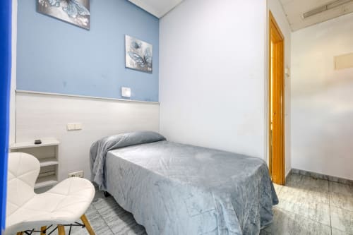 Habitación privada pequeña con cama individual, paredes azules y blancas, escritorio y puerta de madera en Hostal El Molino de Collado Villalba