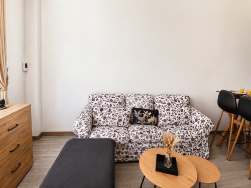 Acogedora sala de estar en Apartamentos El Calón Playa con sofá floral, muebles de madera y mesa de centro redonda en Cuevas del