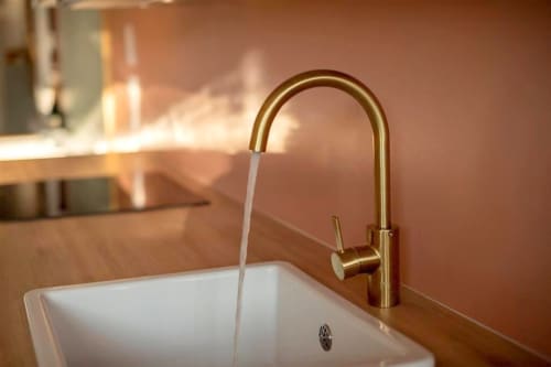 Robinet doré avec eau coulante dans un lavabo blanc de la salle de bain du loft des Gîtes Saint Valery En Caux