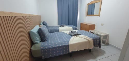 Modernes Schlafzimmer im Alquila en Canarias in El Médano mit Doppelbett, blauer Bettwäsche, Holzkopfteil, Spiegel und Küstenblick