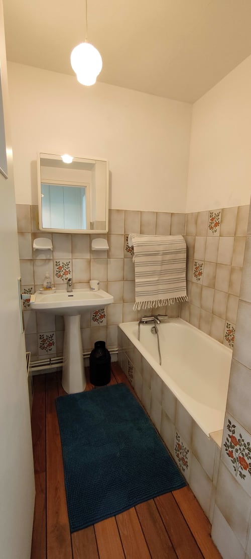 Salle de bains de Mer et Maisons avec carrelage beige, lavabo sur piédestal, baignoire et plancher en bois à La Trinité sur Mer