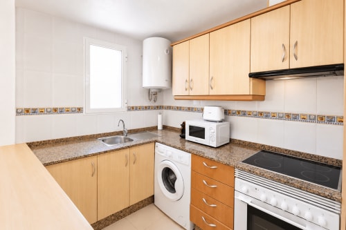 Cocina moderna en Apartamentos El Calón Playa con gabinetes de madera, encimeras de granito, lavadora, placa eléctrica y