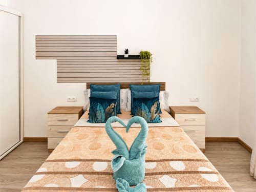 Dormitorio moderno en Apartamentos El Calón Playa con cabecero de madera, almohadas turquesas y cisne de toalla en Cuevas del Almanzora