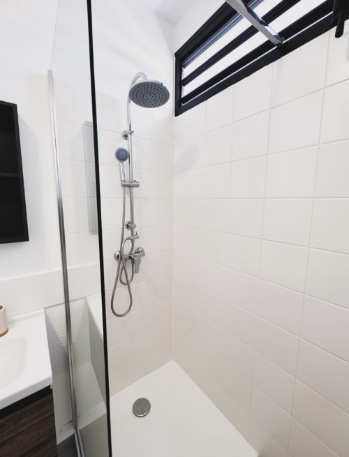 Salle de bains moderne avec pommeau de douche cascade, douchette manuelle et carrelage blanc à l'appartement Maisons En Or de Cayenne