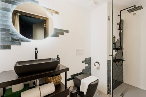 Banheiro moderno em hotel no Porto com cuba preta, espelho iluminado, chuveiro tipo chuva e detalhes em azulejos escuros