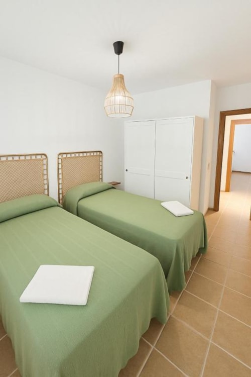 Dos camas individuales con colchas verdes en apartamento moderno de Rural La Palma en El Hierro, con lámpara colgante tejida y decoración blanca
