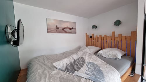 Cozy bedroom at Ô LOCH apartment in La Fôret-Fouesnant with wooden headboard, white bedding, and coastal wall decor
