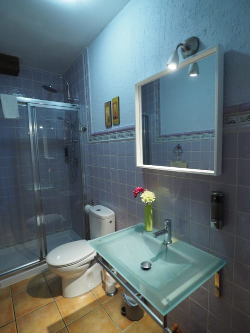 Baño moderno con ducha de cristal, lavabo verde, espejo iluminado y paredes de azulejos grises en apartamento rural