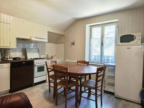 Ampio spazio cucina-sala da pranzo nell'appartamento di Ceillac con tavolo in legno, stufa e vista sulle montagne attraverso le porte in vetro
