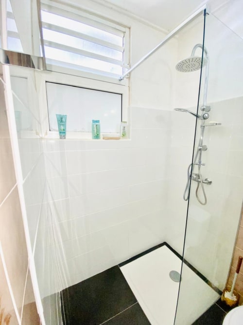 Salle de bain moderne avec douche pluie, paroi vitrée et étagère intégrée à l'appartement Maisons En Or à Cayenne