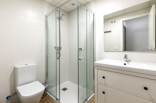 Modern bathroom at Residencia Demar hotel in Godella with glass shower enclosure, white vanity, toilet, and mirror