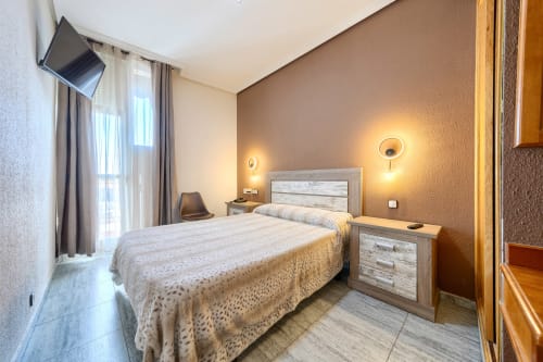 Moderno dormitorio doble en Hostal El Molino de Collado Villalba con cama, mesitas de noche, iluminación cálida y balcón privado