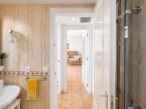 Bathroom with beige tile walls, yellow towel, and shower in Apartamentos El Calón Playa, Cuevas del Almanzora