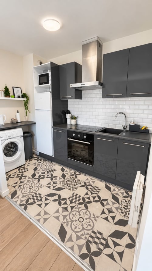 Cuisine moderne avec armoires foncées, dosseret en carrelage blanc, carreaux de sol à motifs et électroménagers inoxydables au Le