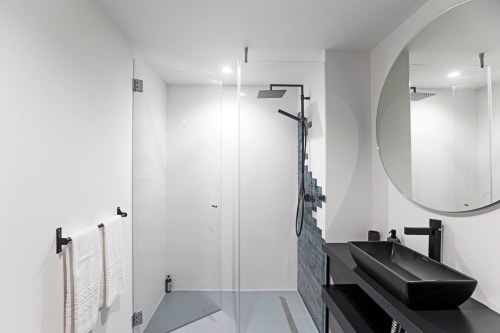 Modern bathroom in Porto hotel with black sink, round mirror, glass shower enclosure, and white walls
