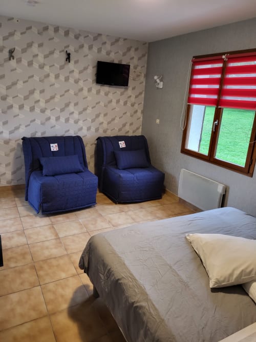 Chambre quadruple spacieuse à l'Hôtel Cheverny avec lit, assises bleues, TV et vue sur le jardin