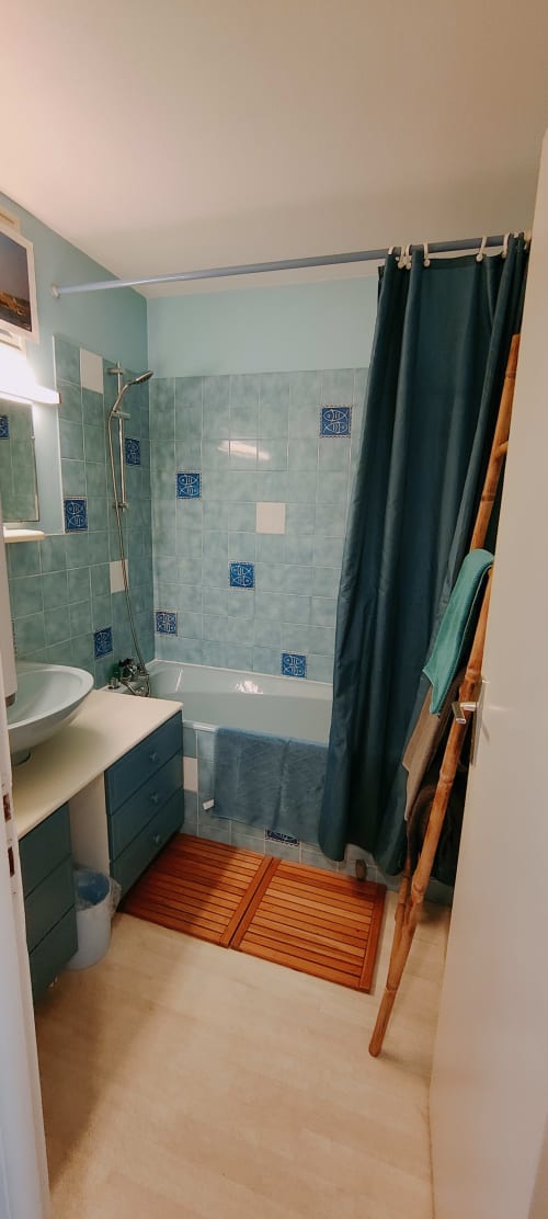 Salle de bain moderne chez Mer et Maisons avec douche en carrelage vert, vasque, tapis de bain en bois et rideau foncé