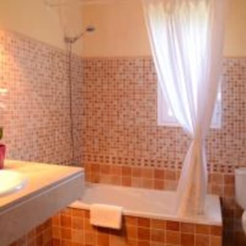 Lujoso baño en villa Las Golondrinas con paredes de azulejos terracota, bañera profunda, cortina blanca y luz natural