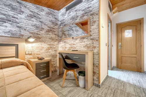 Habitación abuhardillada doble del Hostal El Molino en Collado Villalba con paredes de ladrillo, techo de madera, cama, escritorio y entrada