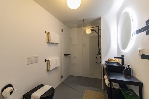 Banheiro moderno em apartamento de hotel no Porto com vaidade preta, espelho iluminado, chuveiro aberto e aquecedores de toalha