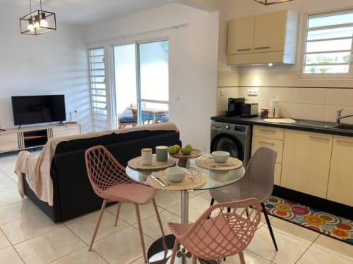 Appartement moderne à Kay Betty avec séjour ouvert, cuisine jaune, coin repas avec table ronde, canapé noir et jardin