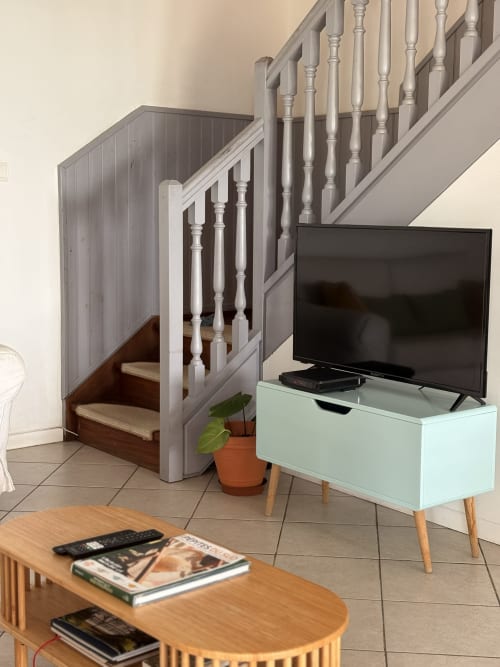 Séjour moderne de villa avec escalier, TV sur meuble menthe, table en bois et plante en pot à La Villa Maraloupia