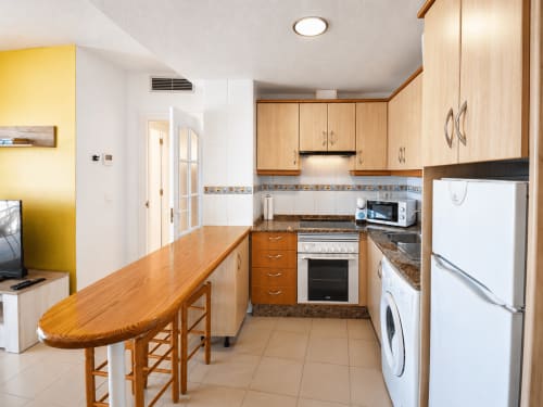 Cocina moderna en Apartamentos El Calón Playa con muebles de madera, electrodomésticos de acero inoxidable y zona de comedor