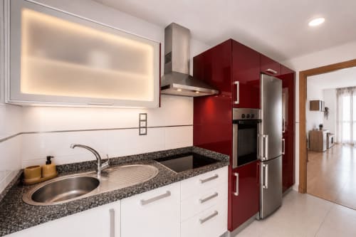 Cuisine moderne dans l'appartement Sara & Gino à Fuerteventura : armoires rouges, plan de travail en granit, appareils en acier inoxydable et