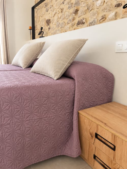 Habitació moderna a l'L'Algars Boutique Hotel de Cáceres amb edredó acolchit púrpura, coixins color crema i taula de nit de fusta