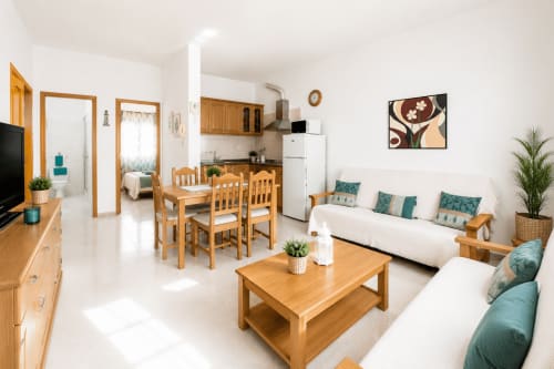 Salon lumineux avec mobilier en bois, murs blancs, touches de bleu canard et cuisine à Corralejo, Fuerteventura