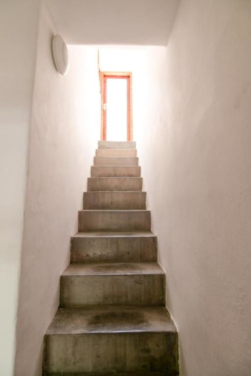 Escalera de hormigón con paredes blancas que sube hacia puerta enmarcada en naranja en Casa 1820, apartamento rural La Palma en Santa Cruz