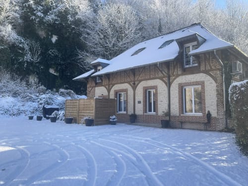 Snow-covered brick villa with half-timbered roof at Les Gites De Flaubert in Le Héron, France, surrounded by winter trees and