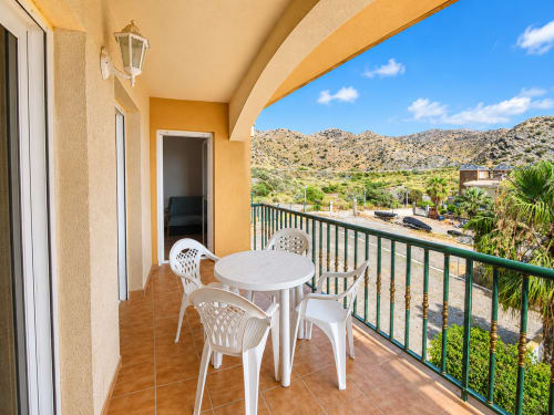 Balcony terrace at Apartamentos El Calón Playa with white table, chairs, mountain views, and green railing overlooking Cuevas