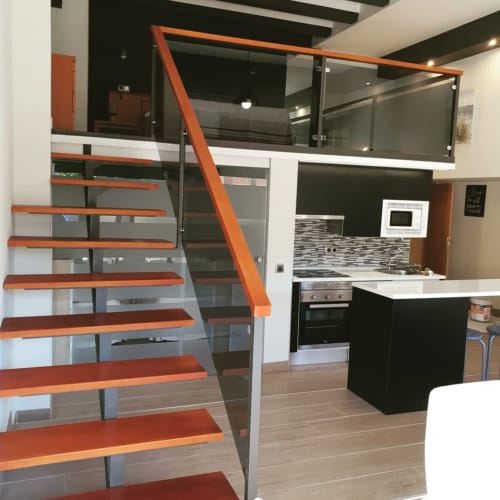 Apartamento moderno en Hostal El Molino con escalera naranja, barandilla de cristal, cocina abierta e isla con encimera negra