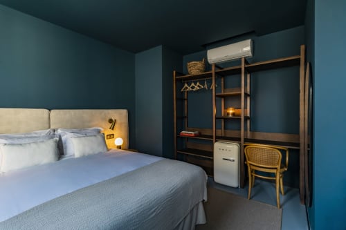 Quarto de estúdio moderno em hotel do Porto com paredes verde-azulado, guarda-roupa em madeira, secretária e roupa de cama branca com vista para a cidade.