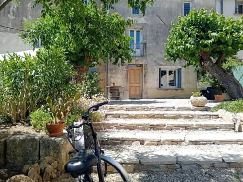 Cour en pierre avec vélo, escaliers, plantes fleuries et maison méditerranéenne à Chez Laure & Marc à Plaissan