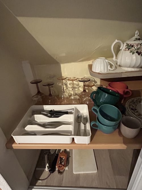 Kitchenette organisée avec rangement blanc pour ustensiles, verrerie, théière et tasses bleu-vert à Hébergement Luxeuil Les Bains