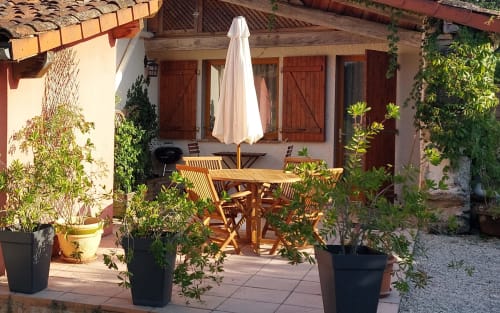 Garden patio at Les Gites de Campardon with wooden dining table, chairs, potted plants, and umbrella in Monties, France
