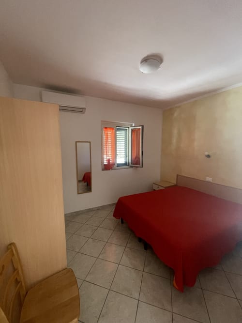 Camera da letto in Villa Angela a Vieste con letto rosso, armadio in legno, pavimentazione in piastrelle, finestra con persiane e aria condizionata