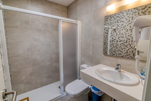 Baño moderno en Las Golondrinas con ducha, lavabo blanco, inodoro y detalles en azulejos de mosaico en Cap d'Artrutx