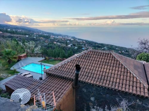 Piscina privada de Villa El Topo y edificio con tejado de barro terracota con vistas a las montañas El Pinillo y el océano al atardecer, La Palma.