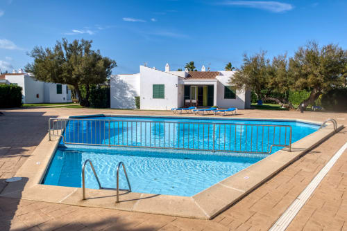 Piscina azul con valla de seguridad en Las Golondrinas Apartamentos Turísticos, Cap d'Artrutx, rodeada de villas blancas