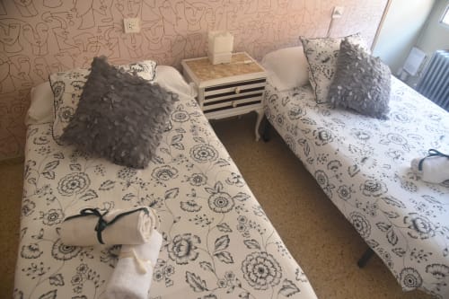 Two twin beds with floral bedding and gray pillows in a Benavente apartment bedroom with patterned wallpaper