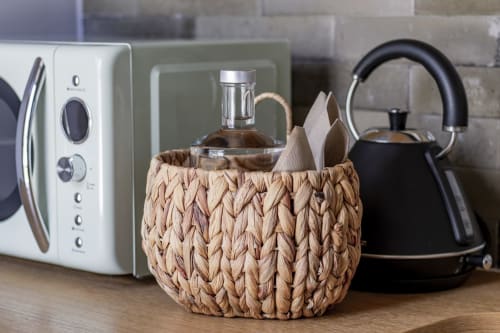 Bancada de cozinha com cesta trançada, micro-ondas branco, chaleira preta e garrafa de vidro no apartamento Benefit Collection Porto