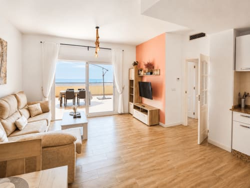 Beachfront apartment living room with sea views, terrace access, tan sofa, wooden floors, and peach accent wall at