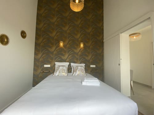 Modern bedroom at La Maison Blanche with white bed, olive patterned headboard, brass wall sconces, and pendant lights in