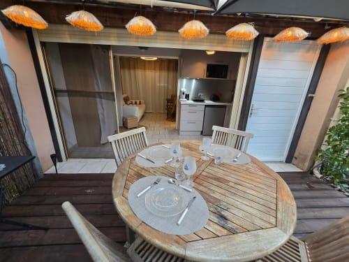 Terrasse de restaurant extérieure à La Montagnette à Cap d'Agde avec table en bois, chaises blanches et chauffages rayonnants surplombant l'appartement