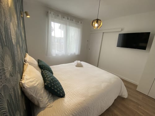 Chambre moderne à La Maison Blanche avec lit blanc, TV murale, luminaire suspendu et vue sur le jardin à Bouguenais